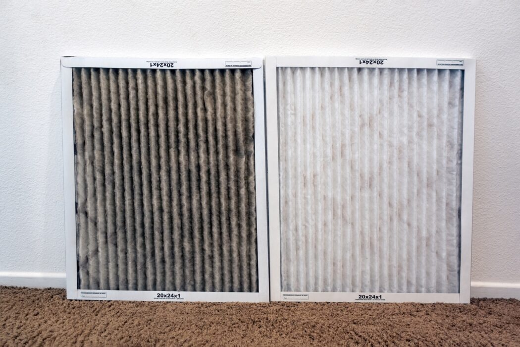 Two air filters sit side by side against a white wall. The left one is discolored, possibly explaining why your AC isn't cooling. Brown carpet below.